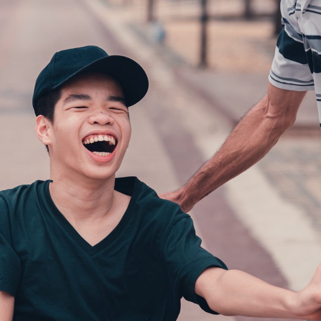 Disabled teenager boy on wheelchair funny face with carer in public places